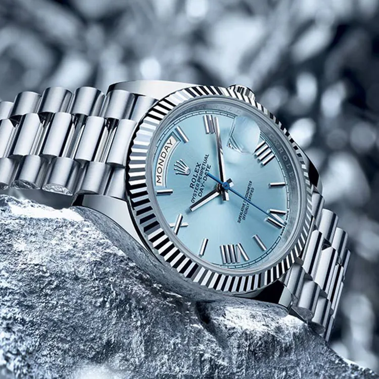 Rolex Day-Date watch with an ice blue dial and silver presidential bracelet on a textured metallic backdrop.