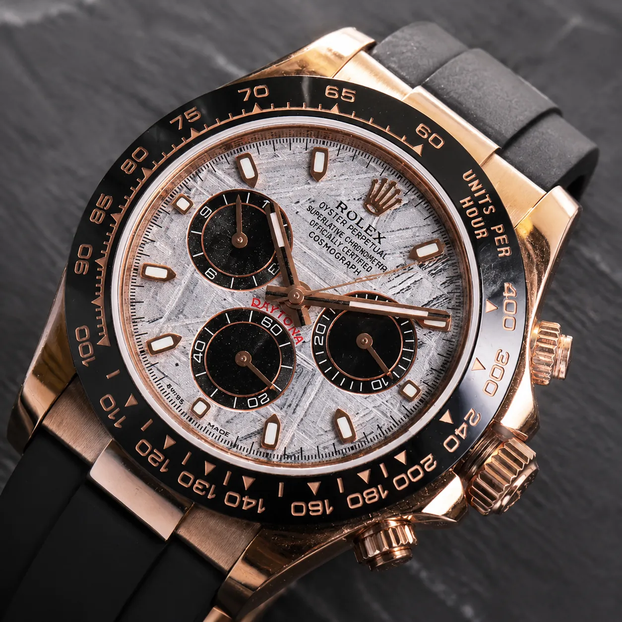 Close-up of Rolex Daytona watch with rose-gold case, black bezel, meteorite dial, and black rubber strap.