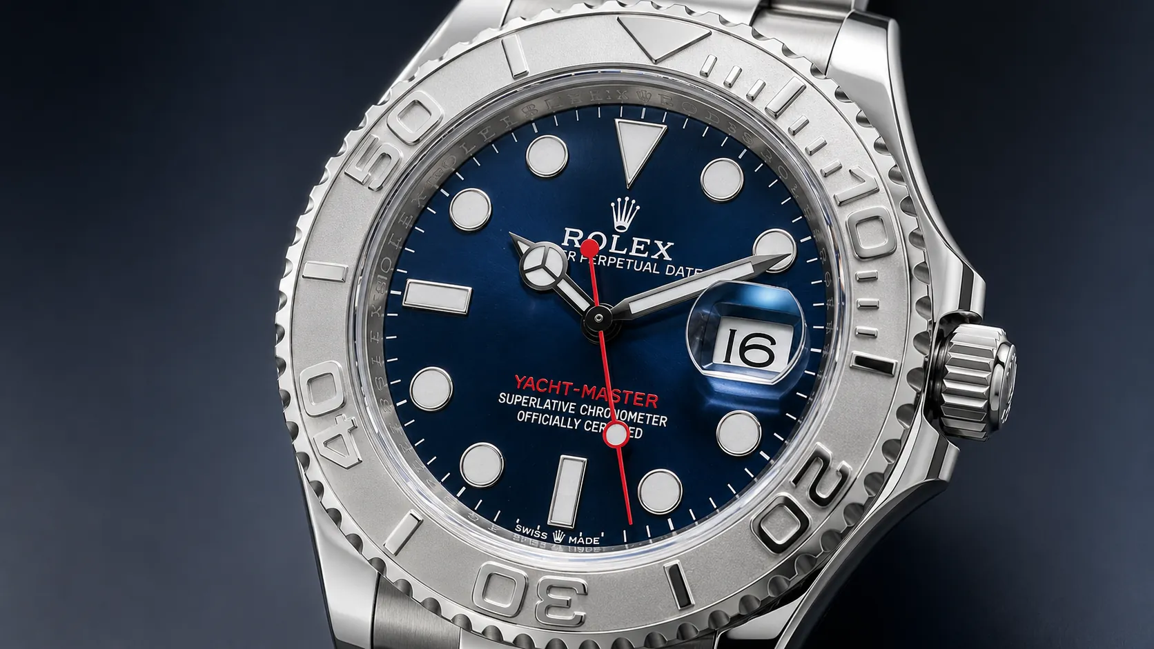 Rolex Yacht-Master close-up with a blue dial, silver bezel, red seconds hand, date magnifier showing 16, and dark studio background.