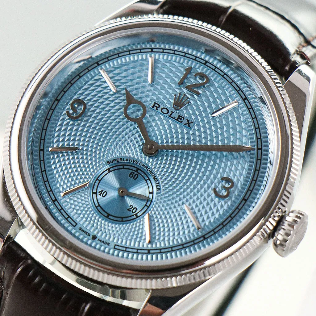 Rolex watch close-up with a light blue textured dial, silver case, small seconds subdial, and dark leather strap.