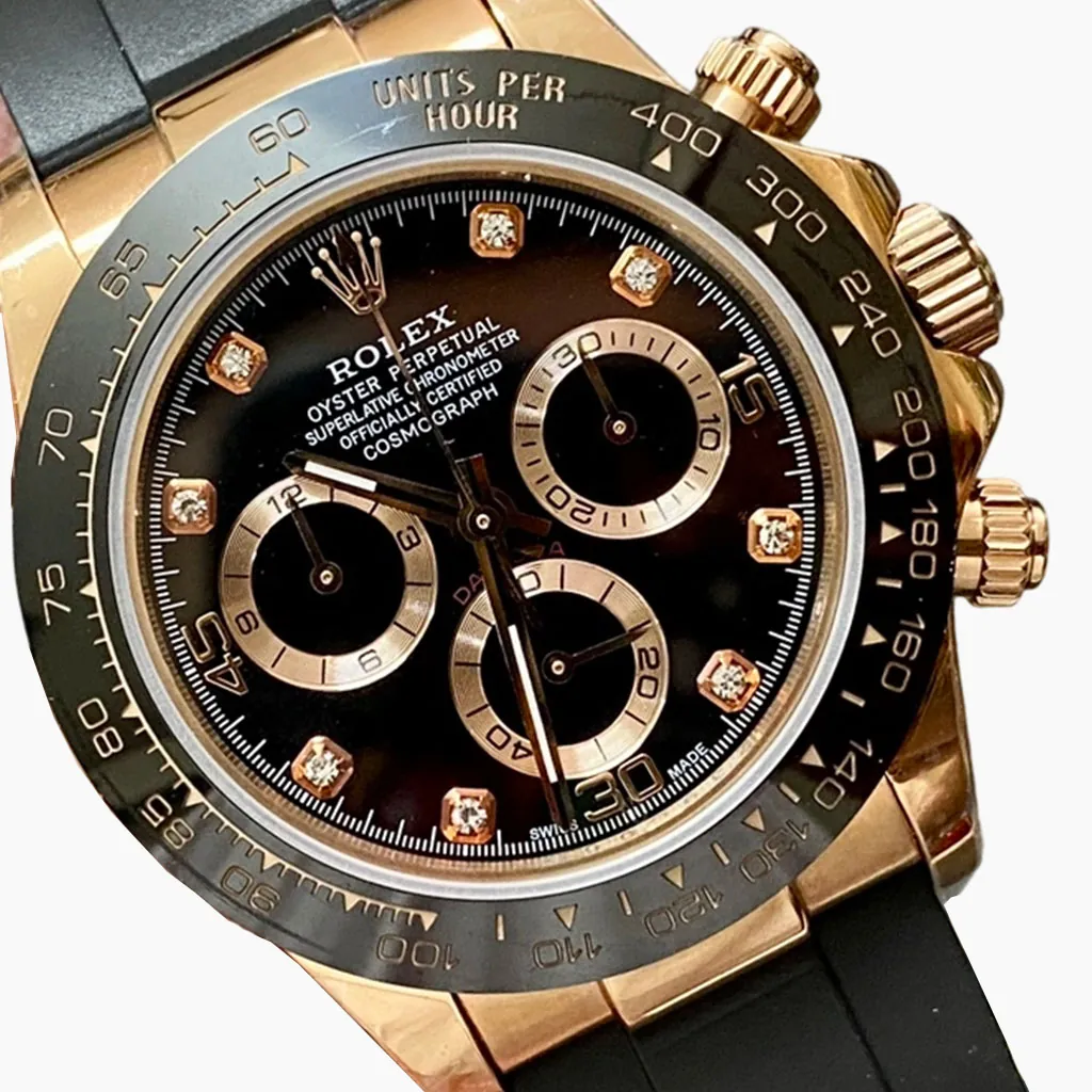 Close-up of a Rolex Daytona-style black and gold chronograph watch, featuring a black dial, diamond hour markers, a rose gold case, and a black rubber strap.