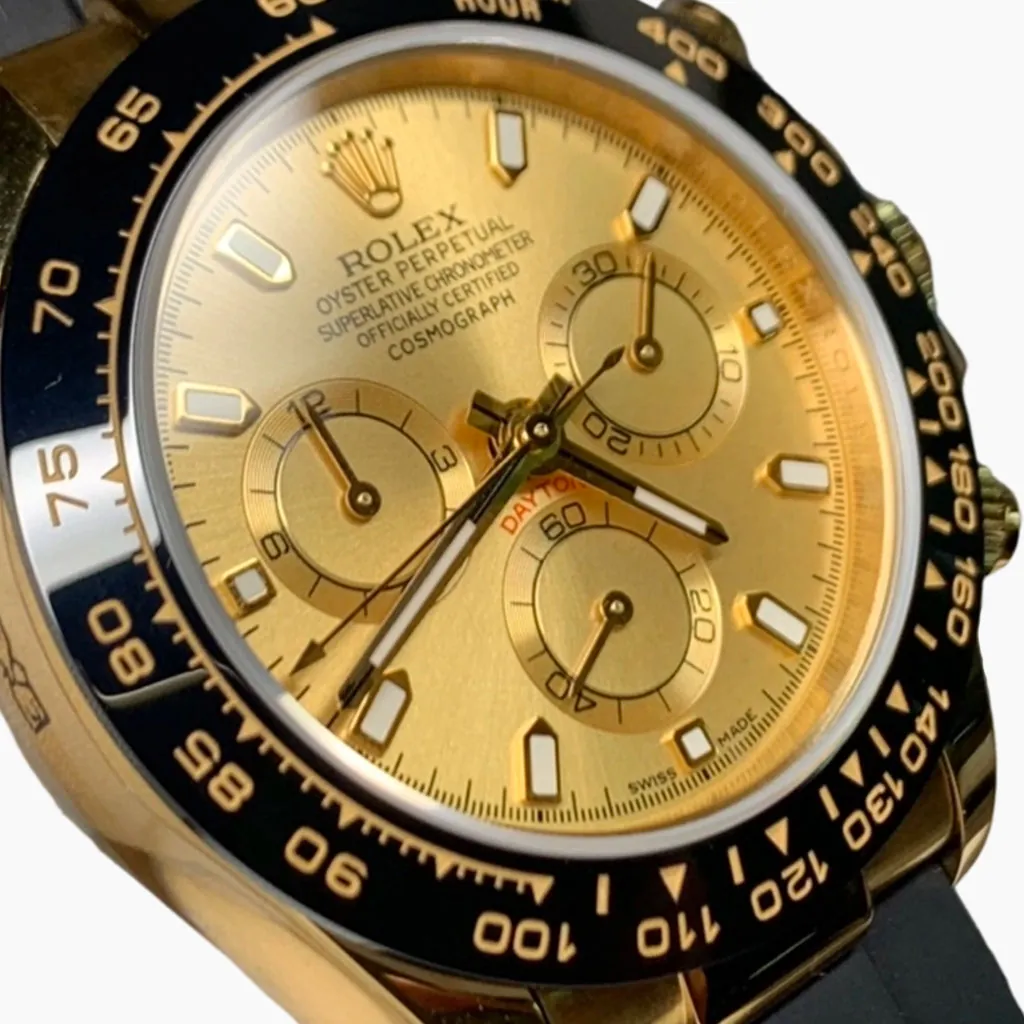 Close-up of a Rolex Daytona-style chronograph with a gold dial, featuring a black tachymeter bezel, a gold case, and a black rubber strap.